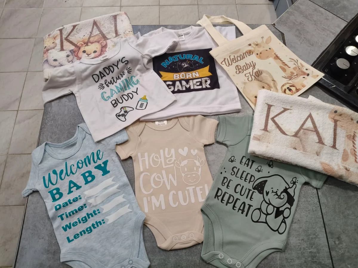 A real completed baby order: personalised onesies, a t-shirt, a tote bag and a towel, all printed with the name Kai