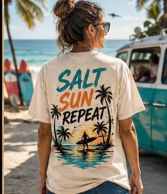 Woman wearing a sand-coloured t-shirt printed with a palm tree and surfer design reading Salt Sun Repeat
